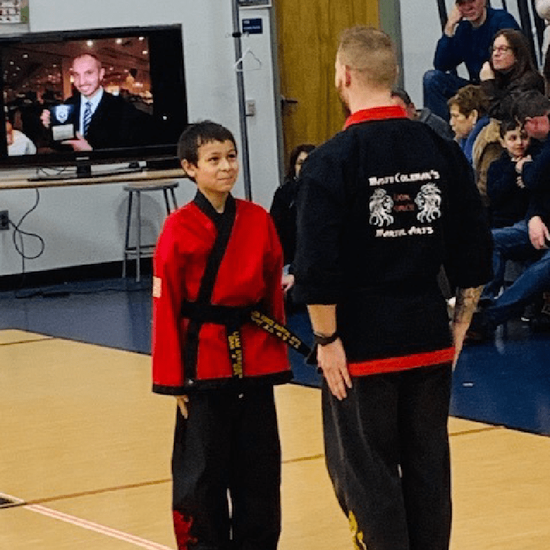 New Project (45) A young boy in a red martial arts uniform standing next to an instructor in a black uniform