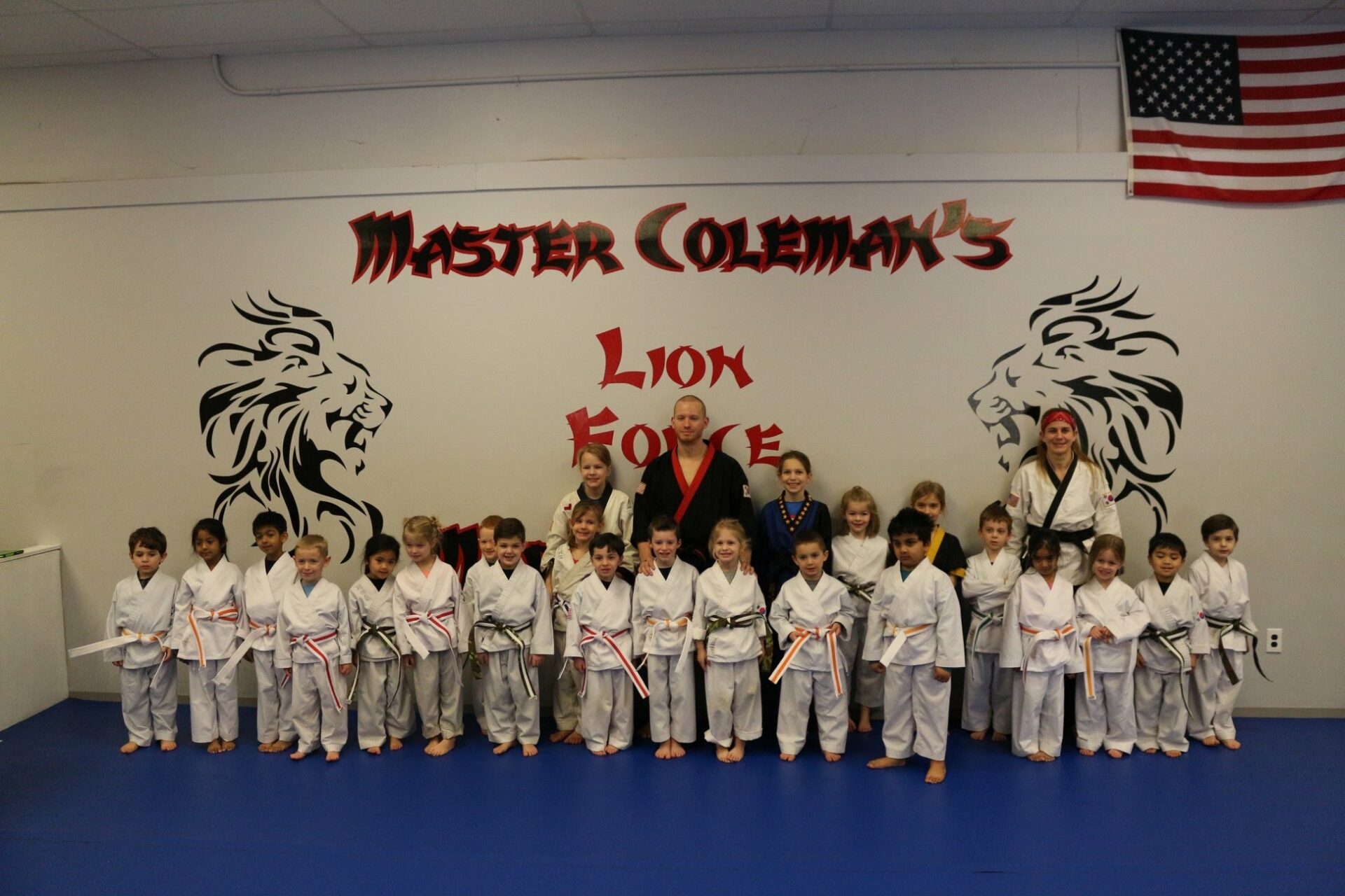 Lion Force Martial Arts Little Lion Program A group of children in martial arts uniforms stand in a row in front of a wall with the text "Master Coleman, Lion Force, SMA"